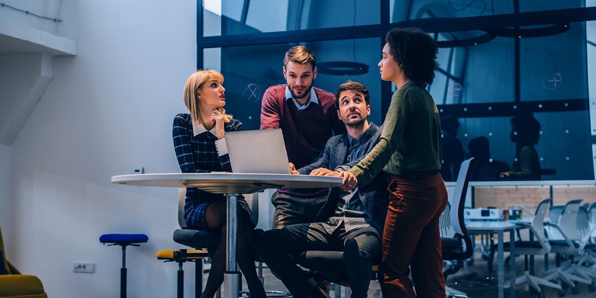 Three individuals gathered around a table with a laptop
